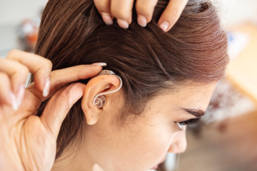Modern digital in the ear hearing aid for deafness and the hard of hearing patients. Young woman with hearing aid indoors. Young woman with hearing aid on light background. Copy space